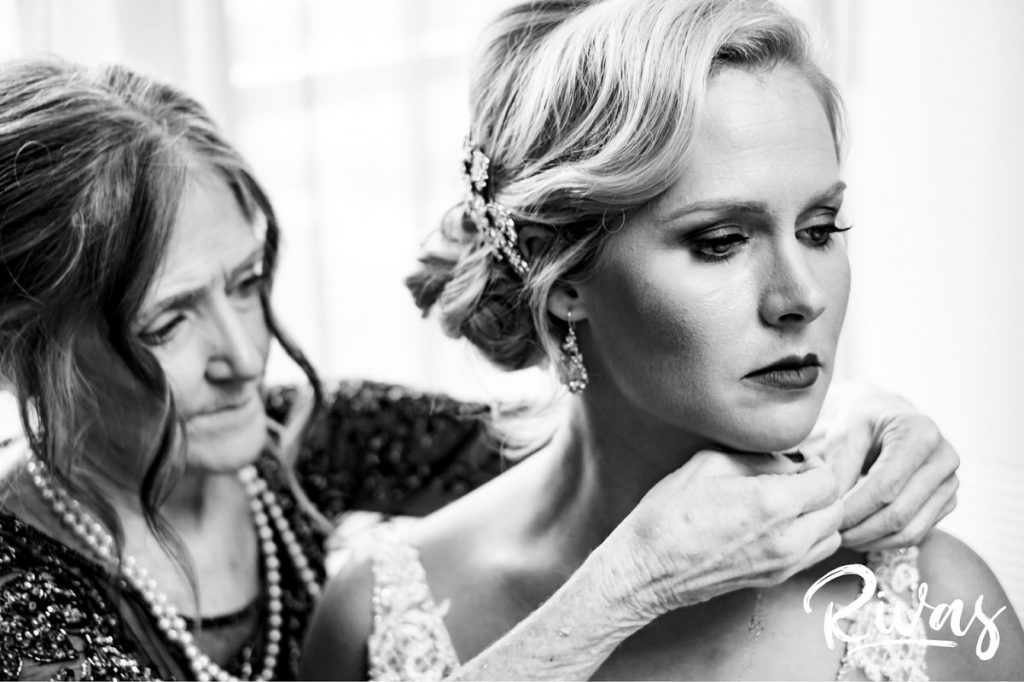 Art Deco Inspired Wedding in Kansas City | A black and white image of a bride's mother clasping her daughter's necklace as she puts it on. 