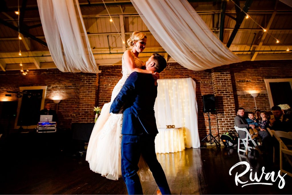 Art Deco Inspired Wedding in Kansas City- A candid, wide picture taken of a groom lifting his bride in his arms during their choreographed first dance at their Californos wedding reception in Kansas City. 