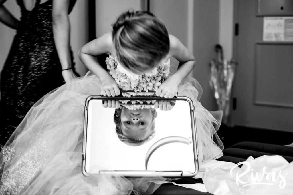 Art Deco Inspired Wedding in Kansas City | A candid, black and white image of a little girl in a full tulle gown leaning over to see her face in a mirror. 