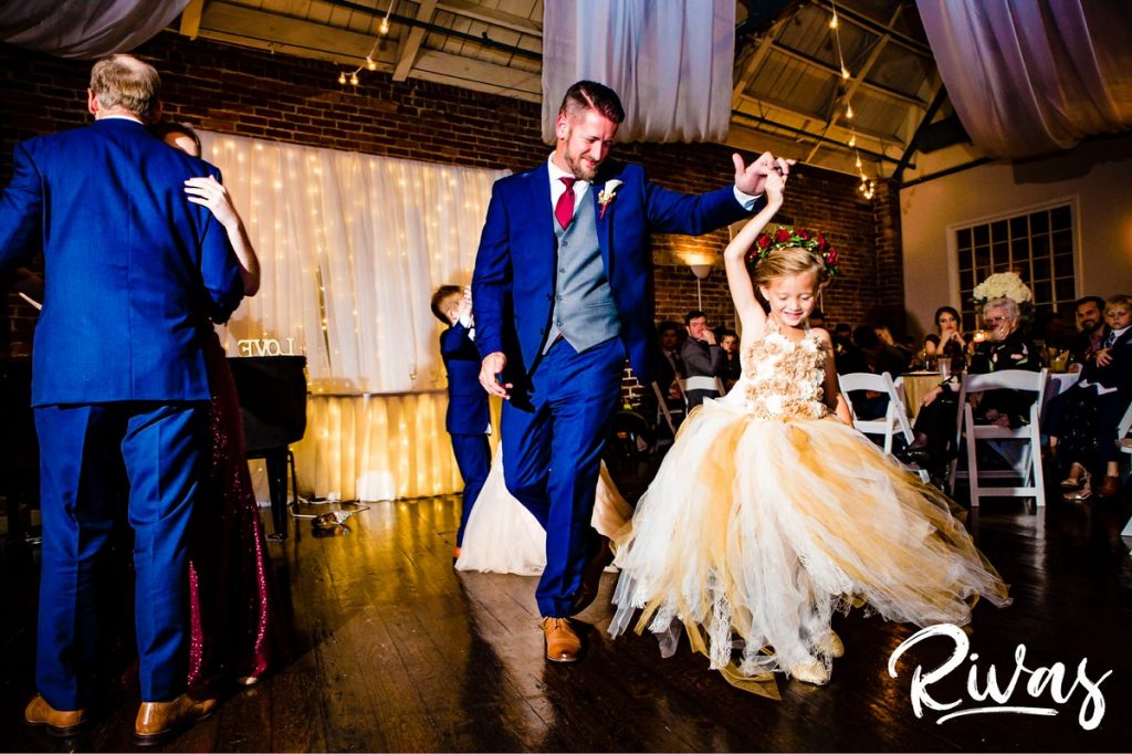 Art Deco Inspired Wedding in Kansas City- A candid picture of a groom twirling his daughter, the flower girl, under his arm in the middle of the dance floor during his wedding reception at Californos. 