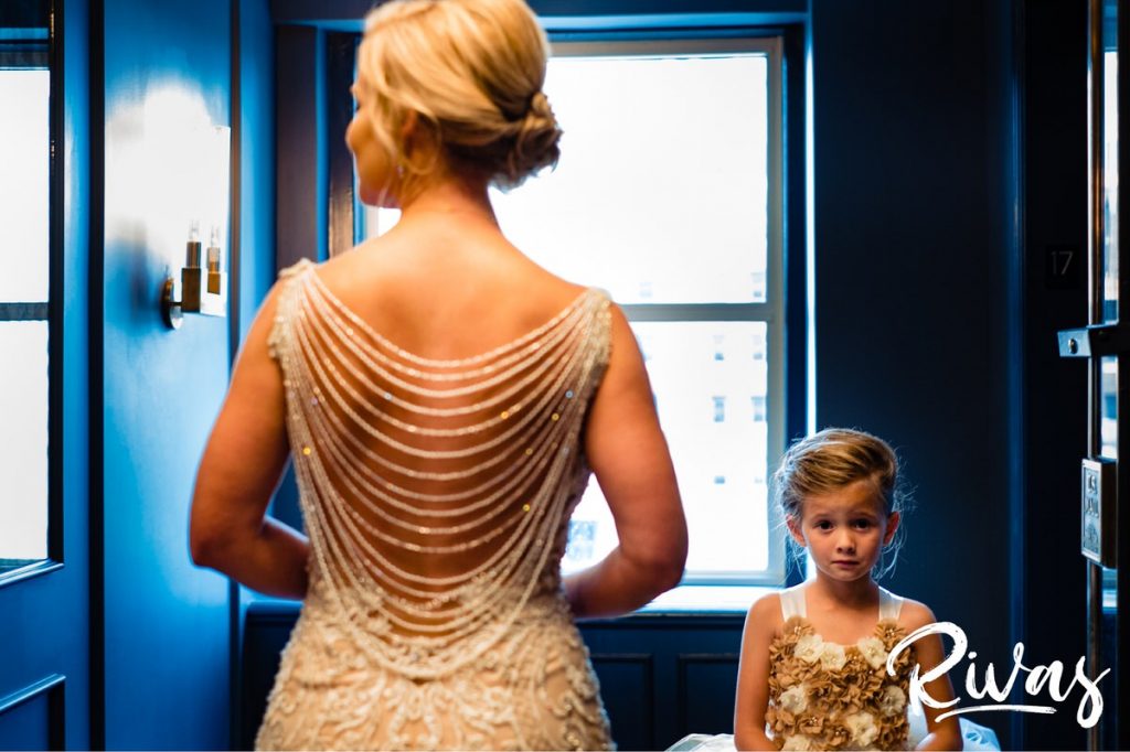 Art Deco Inspired Wedding in Kansas City | A candid picture taken as a bride and flower girl are walking to an elevator. The bride's back is to the cameera, and the little girl is making a funny face at the camera. 