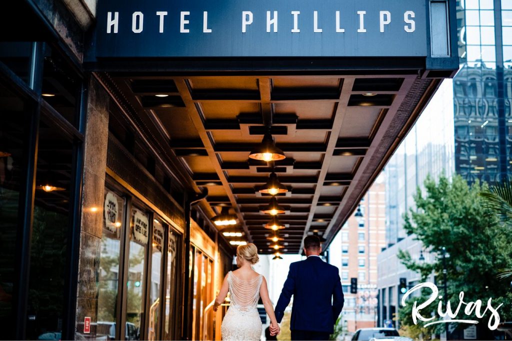 Art Deco Inspired Wedding in Kansas City | A wide image of a bride and groom taken as they walk away from the camera, holding hands, underneath the Hotel Phillips overhang in downtown Kansas City on their wedding day. 