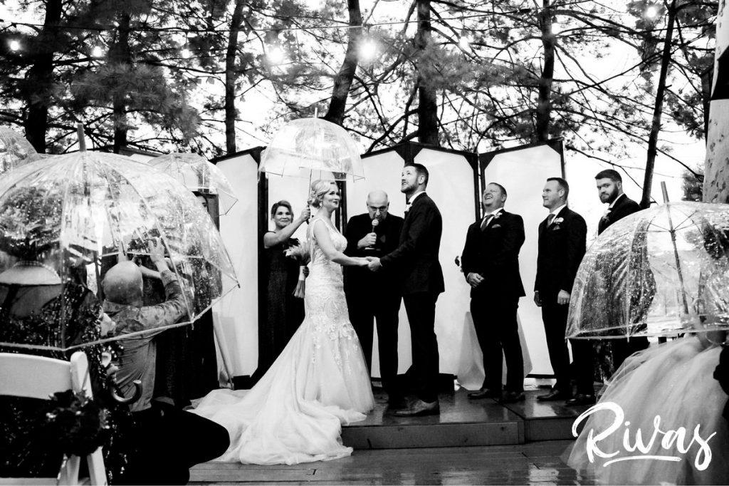 Art Deco Inspired Wedding in Kansas City | A black and white picture of a bride and groom looking to the sky as rain falls during their rainy outside wedding ceremony at Californos. 