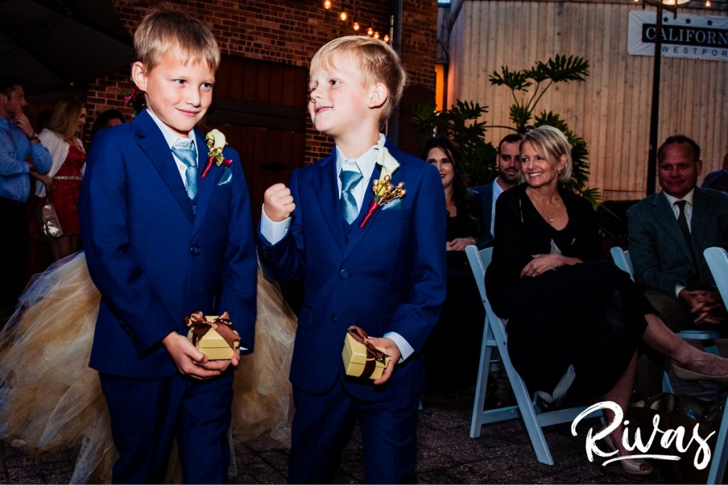 Art Deco Inspired Wedding in Kansas City | A candid picture of two ring bearers in blue suits walking down the aisle and pumping their arms in celebration during their parents' outdoor wedding ceremony at Californos. 