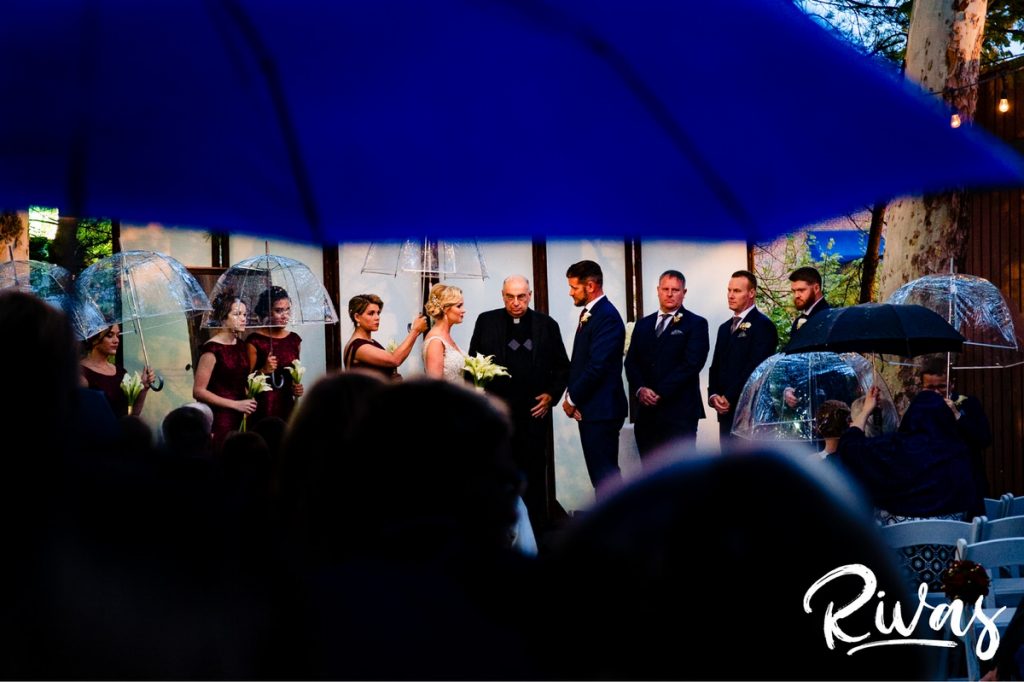 Art Deco Inspired Wedding in Kansas City | A picture taken from under a blue umbrella of a wedding ceremony taking place outside in the rain at Californos. 