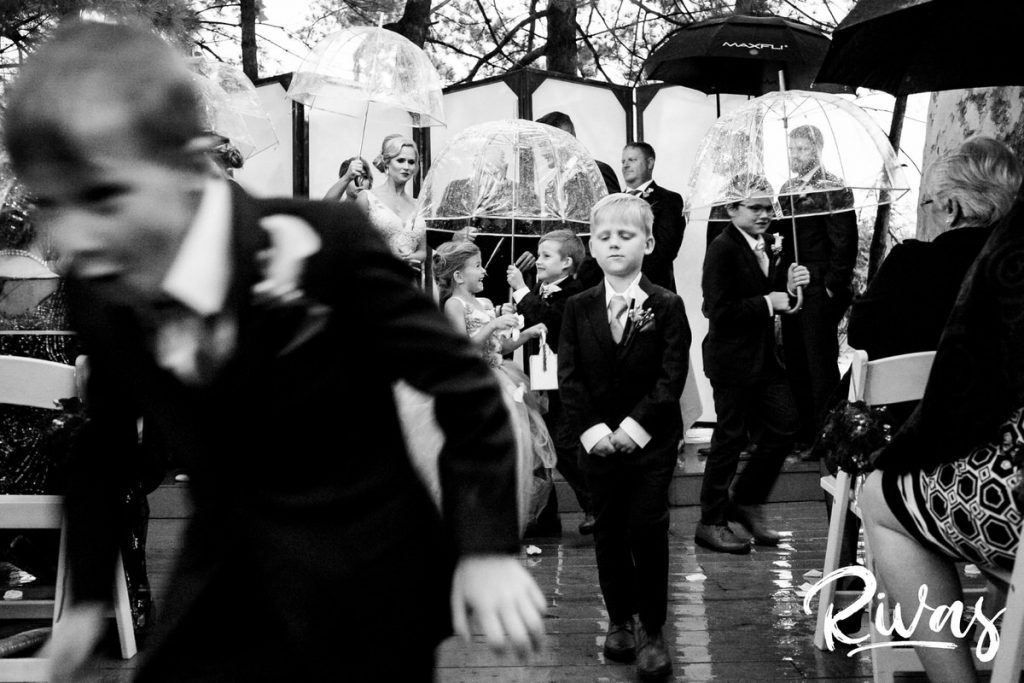 Art Deco Inspired Wedding in Kansas City- A candid, close-up picture of a group of 6 children holding clear umbrellas as they stand with their parents during their outside wedding ceremony at Californos in the rain. 