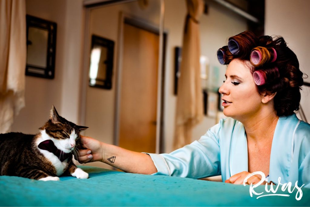 Downtown KC Library Wedding | A candid picture of a bride in her turquoise robe with pink curlers in her hair scratching her cat on the morning of her wedding day. 