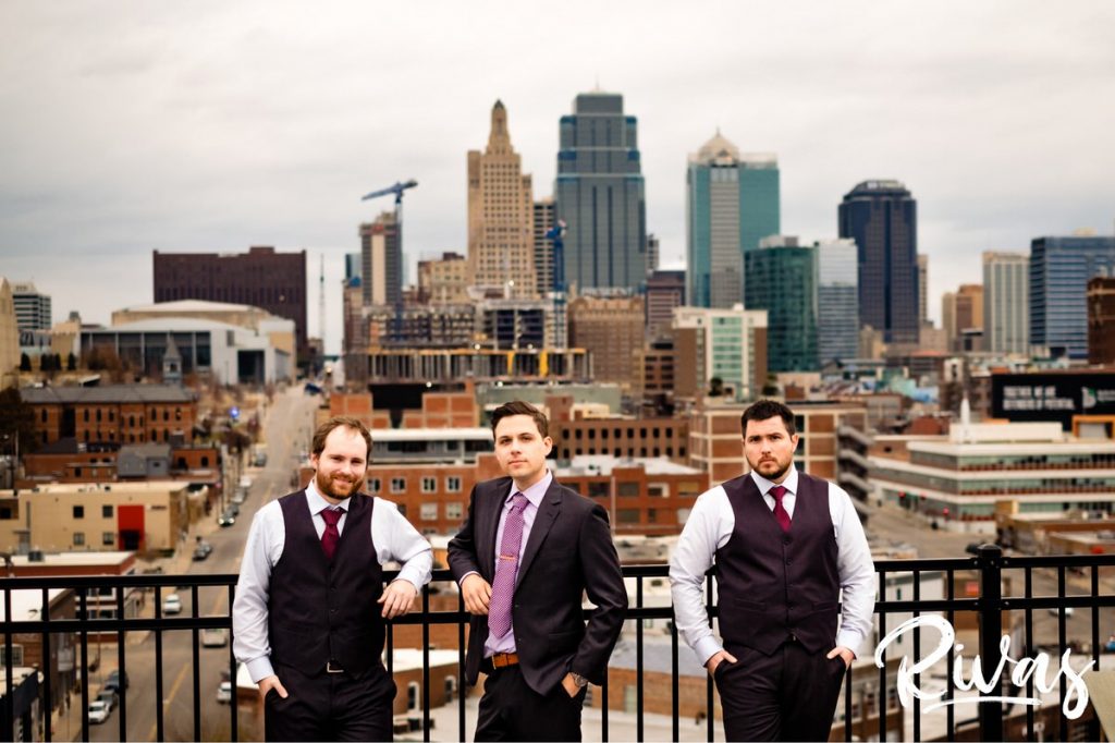 Downtown KC Library Wedding | A portrait of a groom and his two groomsmen in gray vests in front of the Kansas City skyline. 