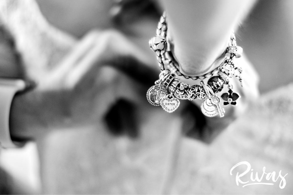 Downtown KC Library Wedding | a detailed black and white picture of a bride's mom's charm bracelet as she's zipping her daughter's wedding dress. 