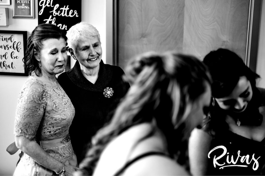 Downtown KC Library Wedding | A candid black and white picture of a bride's mom and grandma watching her daughter put on their wedding dress on the morning of her own wedding. 