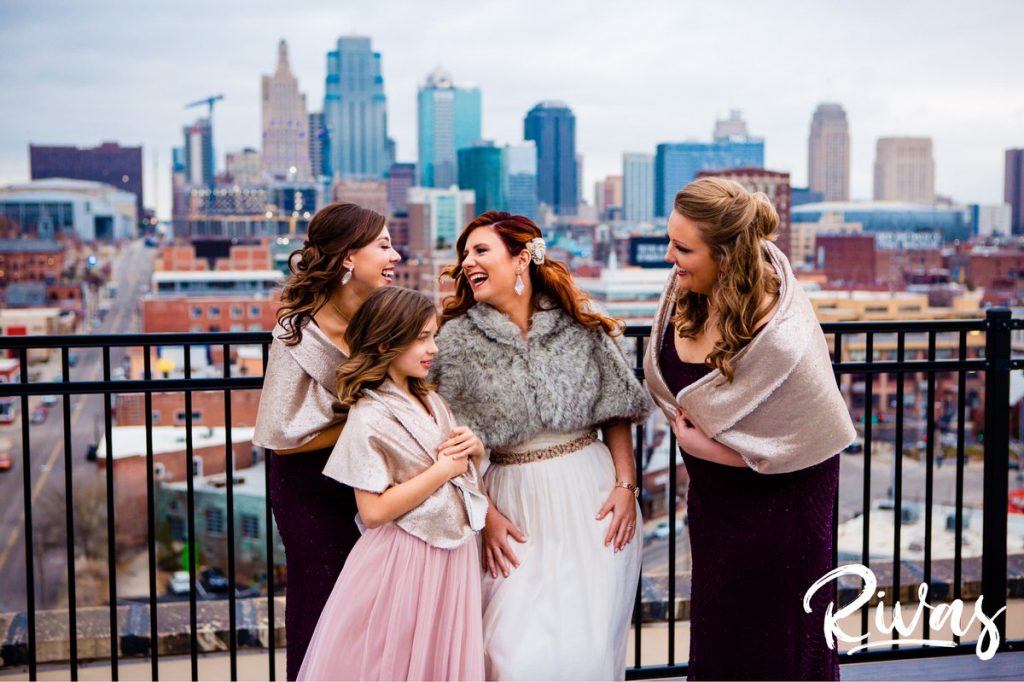 Downtown KC Library Wedding | A candid portrait of a bride and her bridesmaids in shawls standing in front of the Kansas City skyline on the morning of her wedding. 