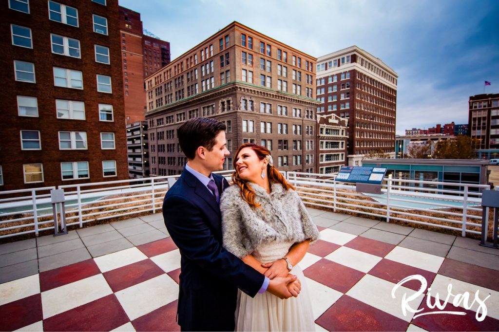 Downtown KC Library Wedding | A colorful, close-up portrait of a bride and groom sharing an embrace as they stand on the rooftop chess board on the Kansas City library on the morning of their wedding day.