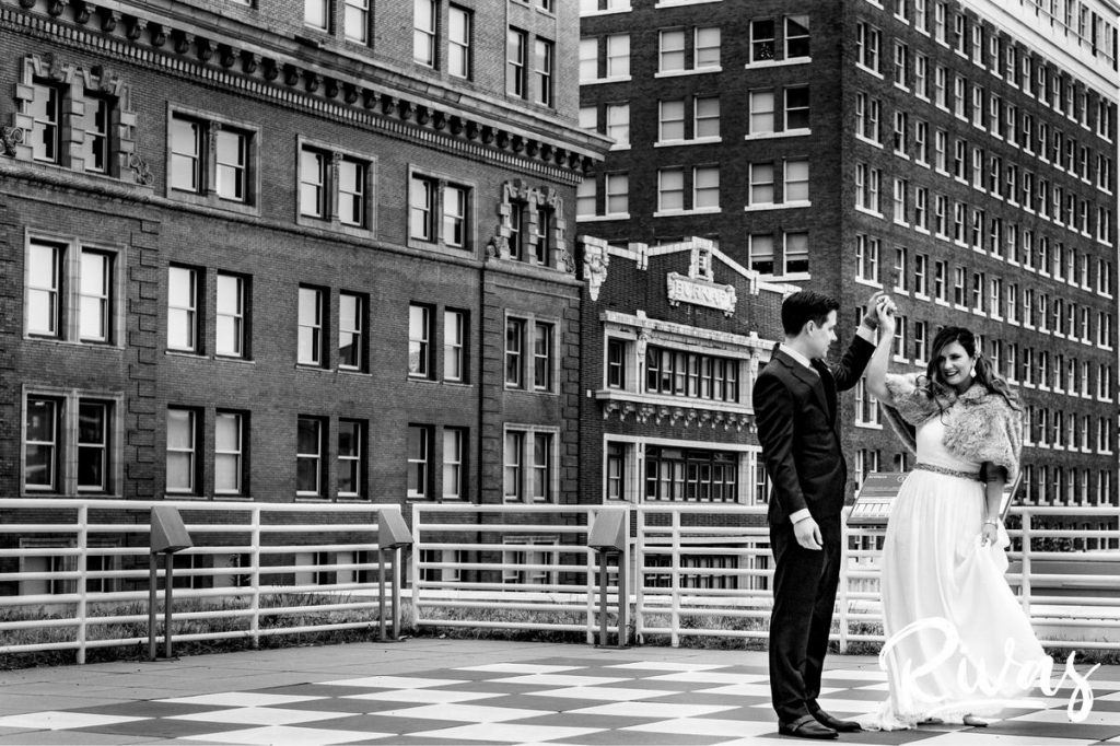 Downtown KC Library Wedding | A candid black and white picture of a groom twirling his bride under his arm on the rooftop of the downtown public library in Kansas City.