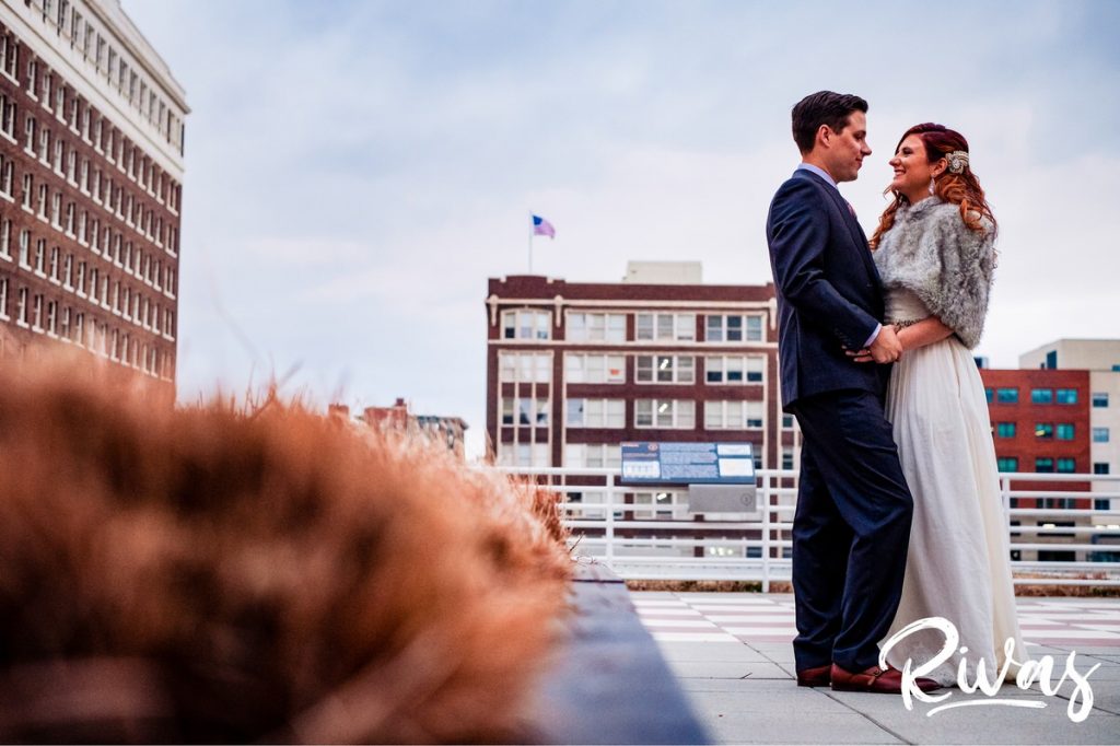 Downtown KC Library Wedding | A colorful portrait of a bride and groom sharing an embrace as they stand on the rooftop of the downtown Kansas City public library on the day of their wedding.