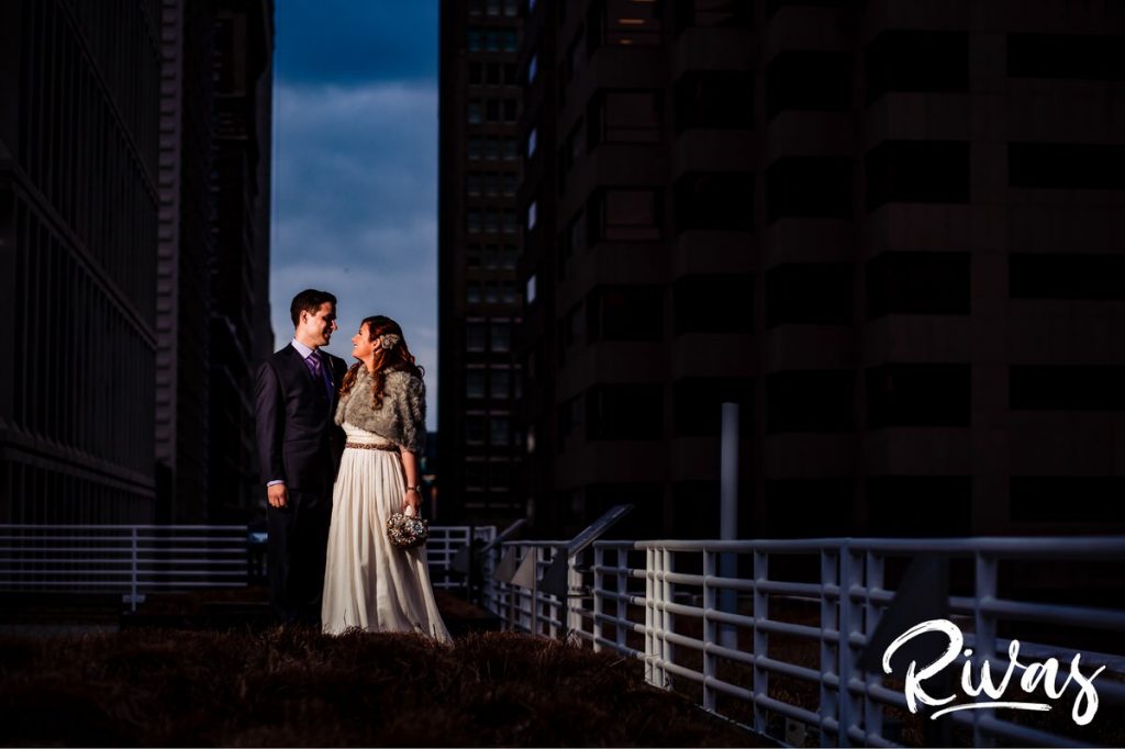 Downtown KC Library Wedding | A colorful portrait of a bride and groom sharing an embrace as they stand on the rooftop of the downtown Kansas City public library on the day of their wedding.