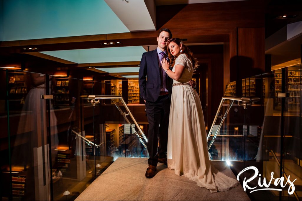 Downtown KC Library Wedding | A portrait of a bride and groom sharing an embrace while standing at the top of a set of stairs in the downtown public library on their wedding day.