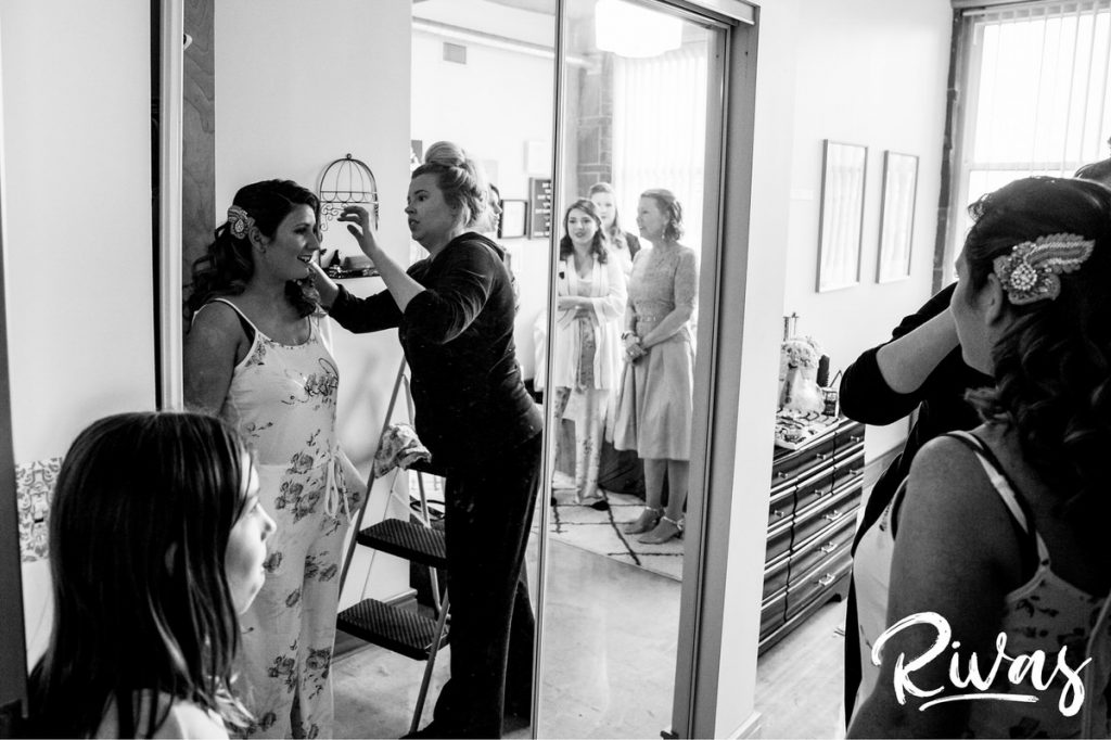 Downtown KC Library Wedding | A candid black and white picture of a bride standing in front of the mirror adjusting her hair as her mom, grandma, and best friends watch. 
