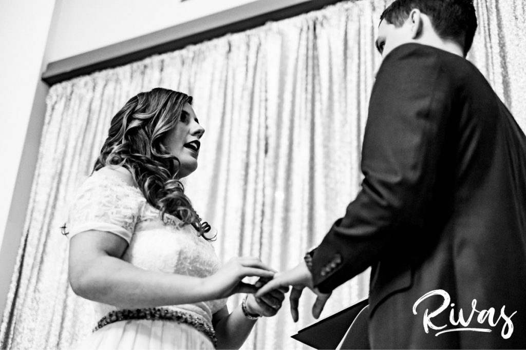 Downtown KC Library Wedding | A close-up black and white picture of a bride putting a wedding band on her groom's finger during their wedding ceremony.