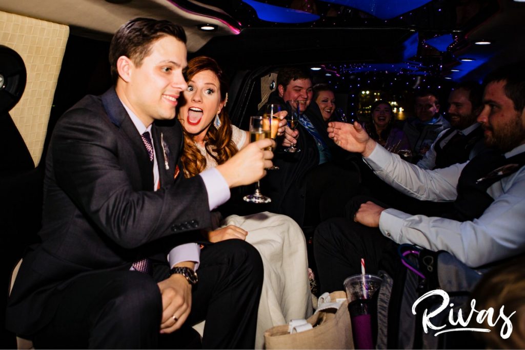 Downtown KC Library Wedding - Rivas Photography | A candid, vibrant picture of a bride and groom toasting with champagne flutes in the back of a packed limo on the evening of their wedding day. 