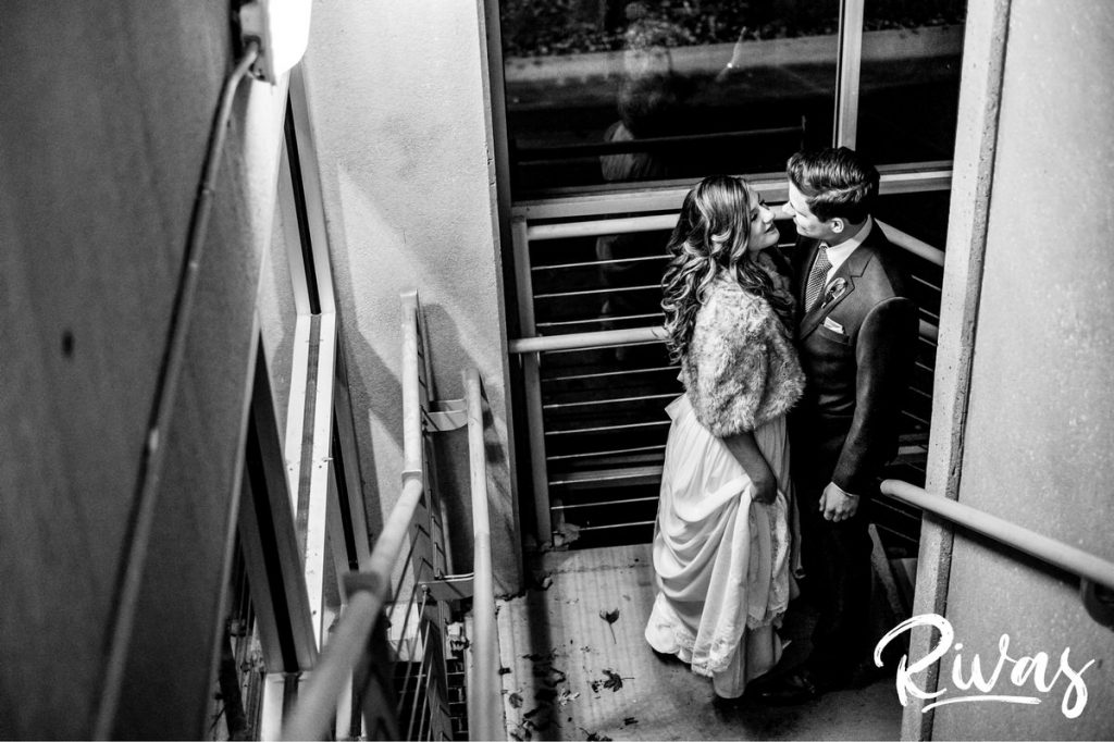 Downtown KC Library Wedding - Rivas Photography | A candid black and white picture of a bride and groom stealing a kiss in the landing of a stairwell outside Boulevard Brewing Company in Kansas City. 