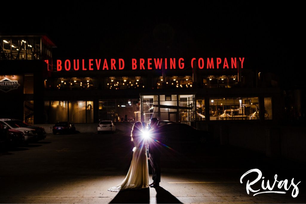 Downtown KC Library Wedding - Rivas Photography | A photo of a bride and groom sharing an embrace in front of the Boulevard Brewing Company Signage at night just before their wedding reception. 