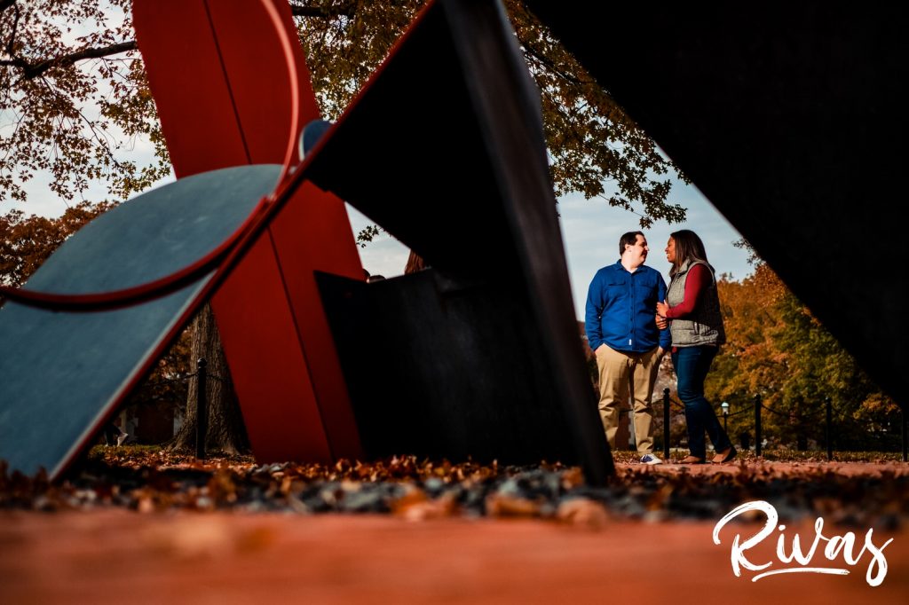 Fall MU Engagement Session | A wide portrait of an engaged couple sharing an embrace and looking into each other's eyes, taken through a statue during their Mizzou engagement session in Columbia.