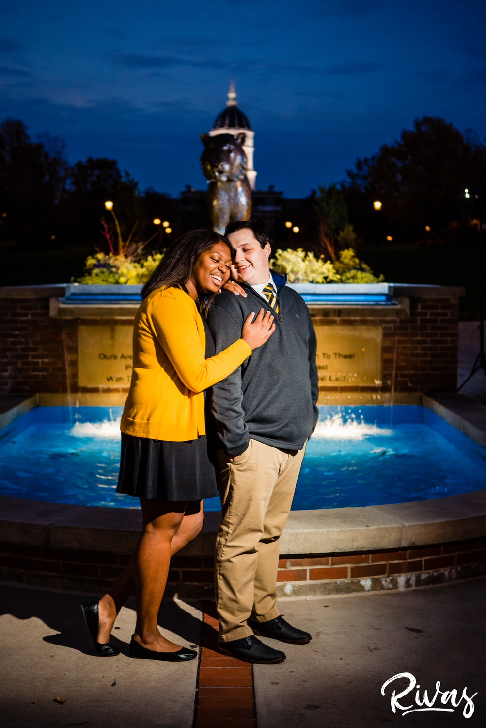 Fall MU Engagement Session | A portrait of an engaged couple sharing an embrace as they stand in front of a bronze sculpture of a tiger on MU's campus during their engagement session.