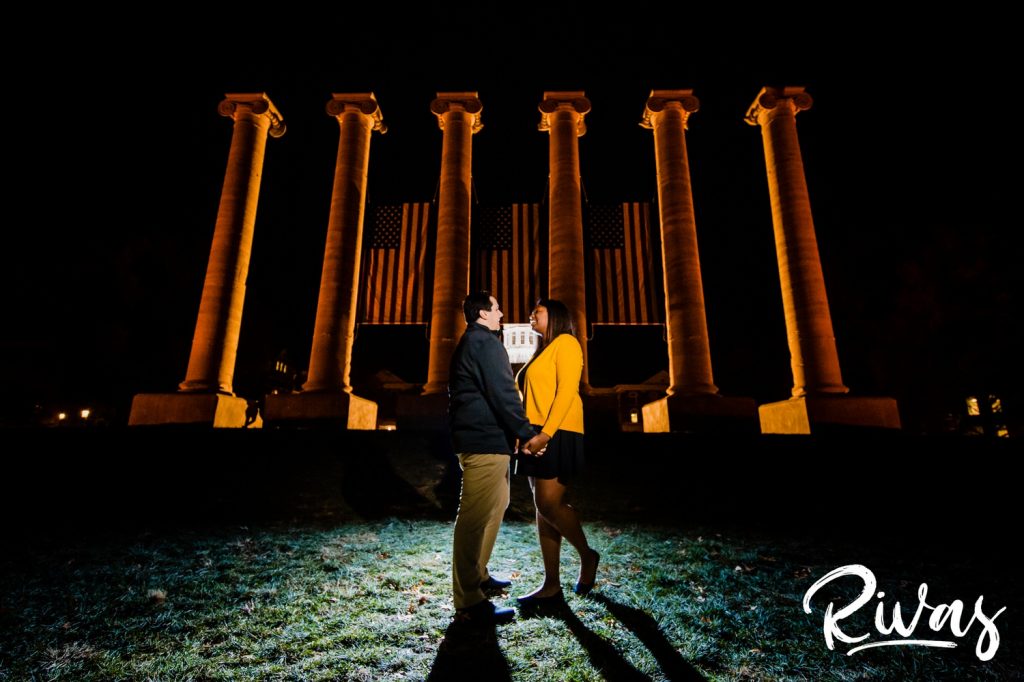 Fall MU Engagement Session | A colorful, nighttime engagement picture of an engaged couple holding hands and laughing together as they stand in front of MU's columns.