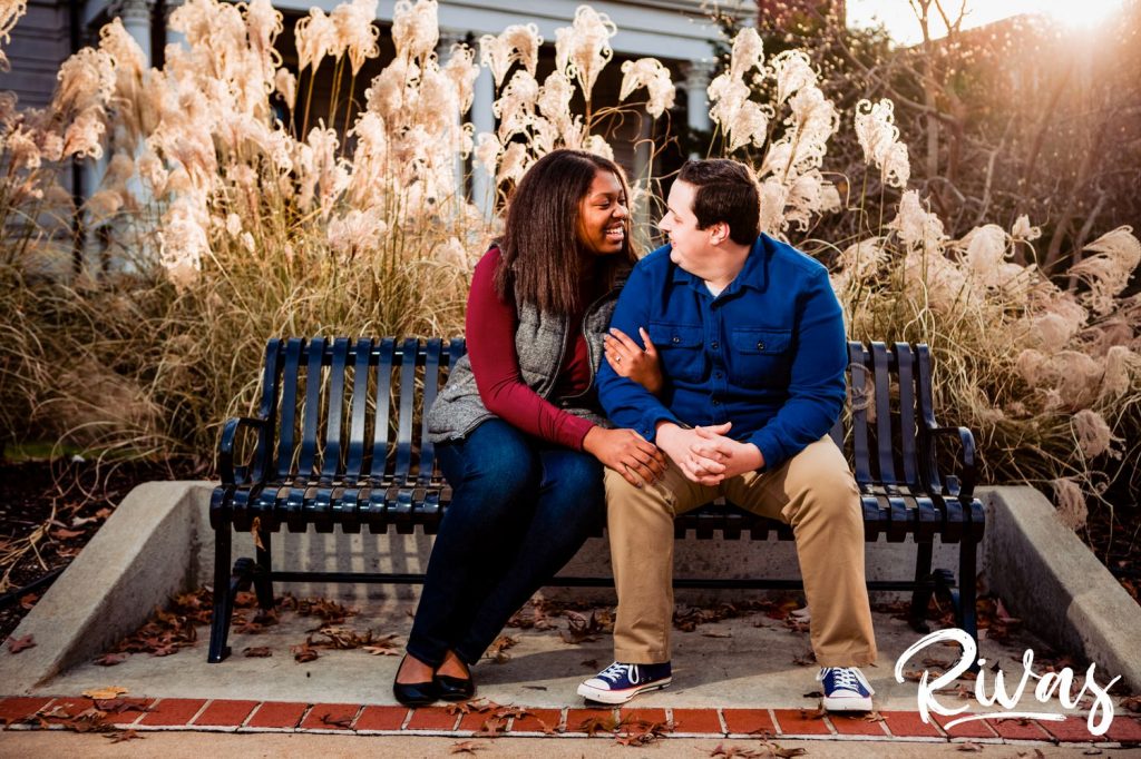 Fall MU Engagement Session | A candid picture of an engaged couple sitting on a bench laughing and embracing each other during their fall MU engagement session.