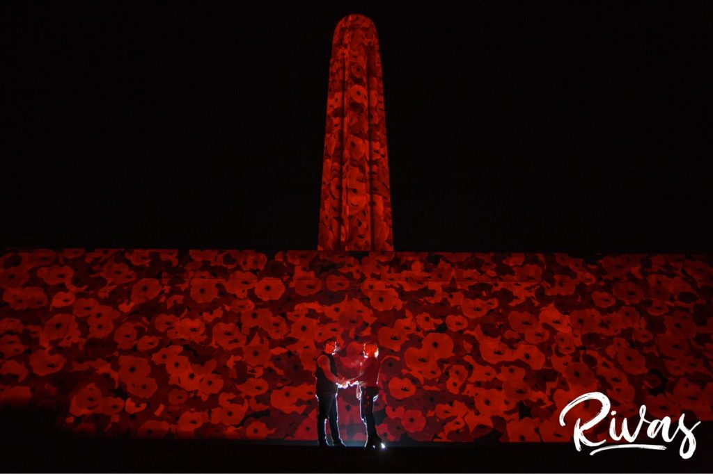 Nighttime Car Engagement Session | A silhouetted picture of an engaged couple sharing an embrace while standing in front of Kansas City's Liberty Memorial, lit up with 5000 poppies in celebration of the Centennial anniversary of the end of World War 1.