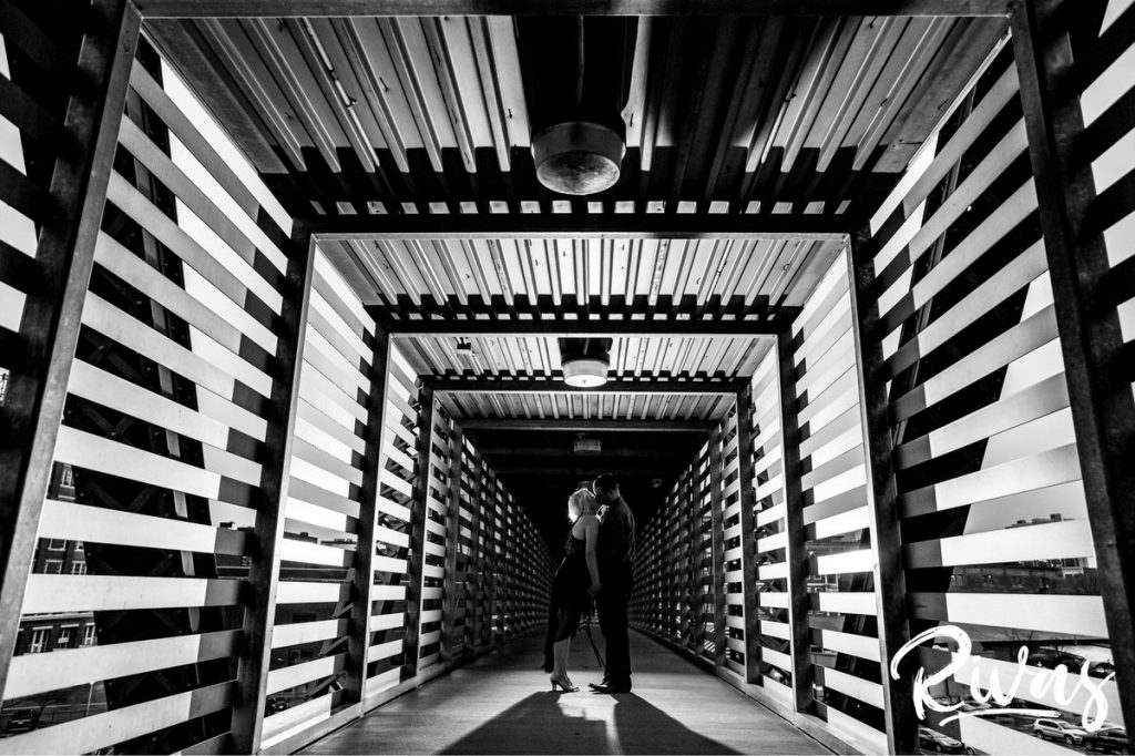 Nighttime Car Engagement Session | A candid black and white picture of an engaged couple dancing down the freight bridge over a set of railroad tracks in Kansas City during their engagement session.