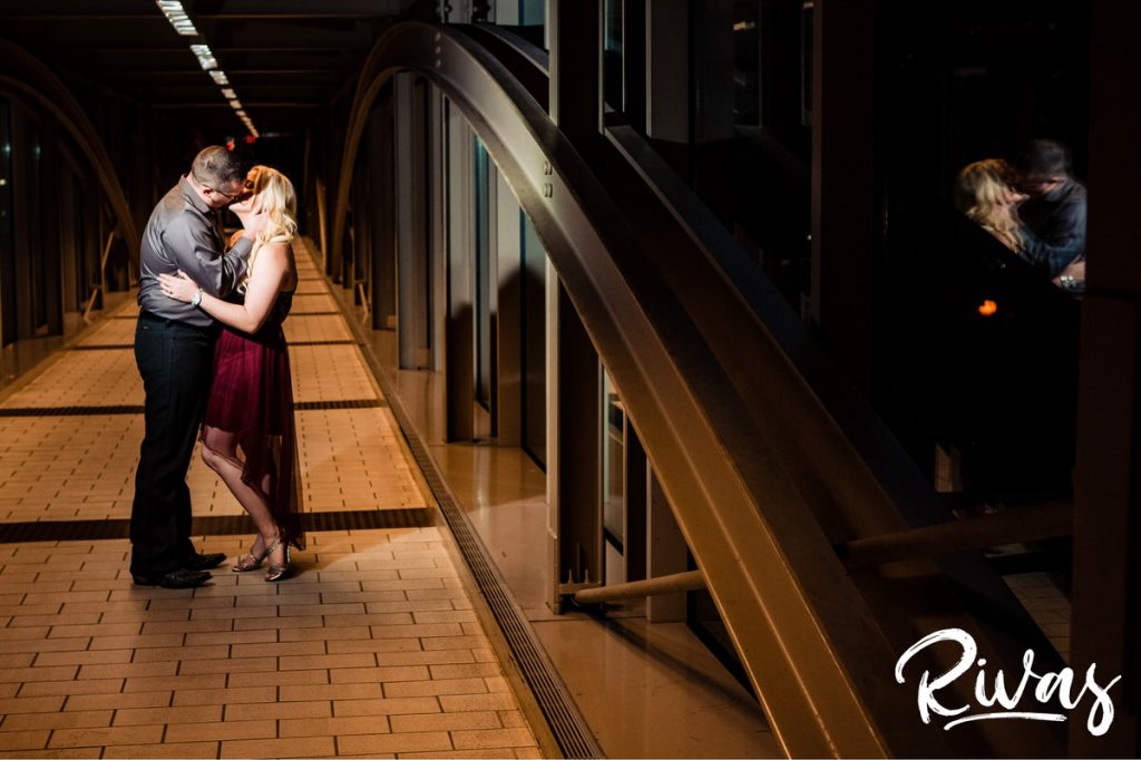 Nighttime Car Engagement Session | A reflective picture of an engaged couple sharing an embrace while standing in The Link walkway that connections Kansas City's Union Station to Crown Center.
