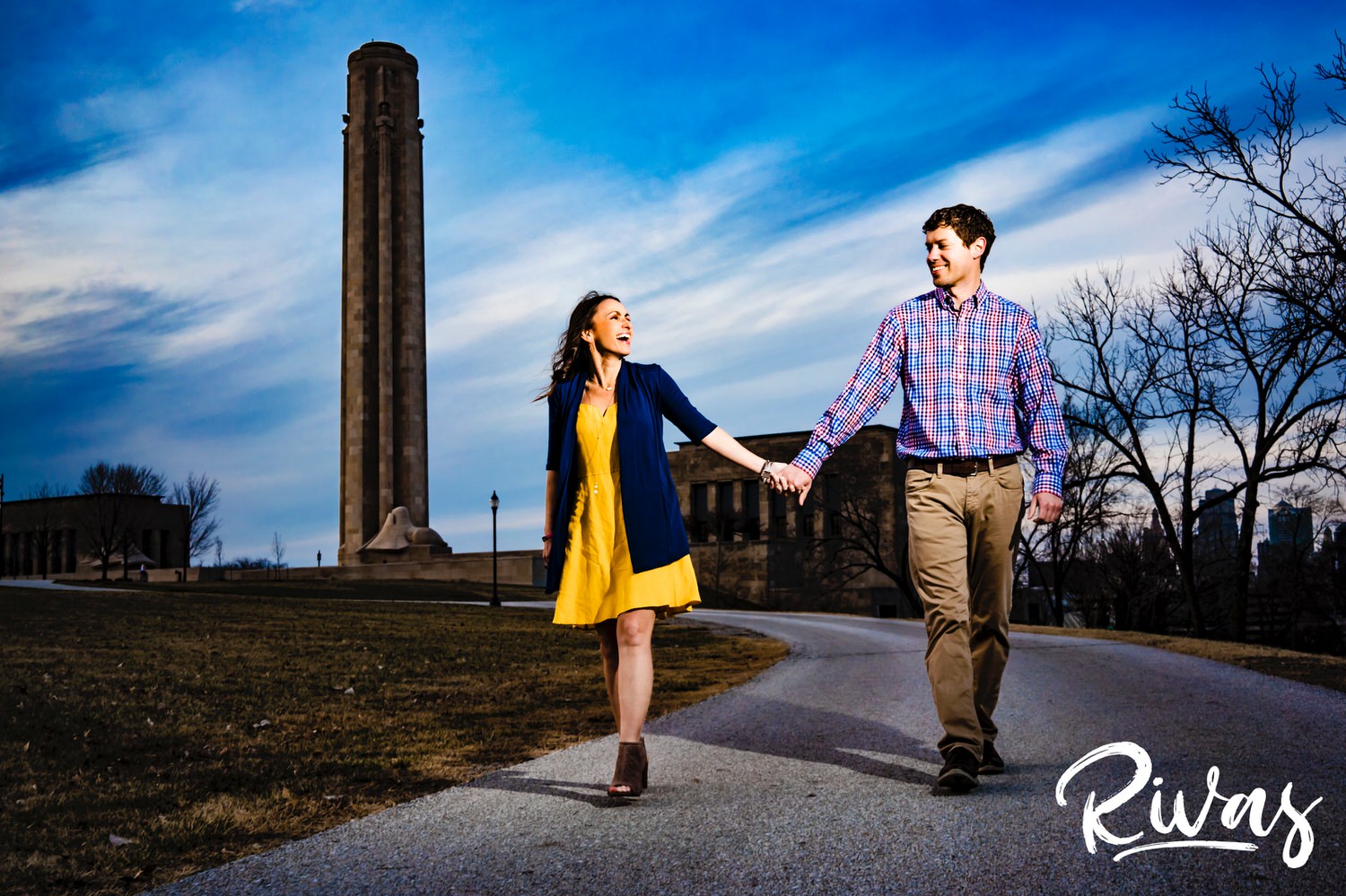 A vibrant, candid picture of an engaged couple holding hands and walking during their sunny engagement session at the end of March at Kansas City's Liberty Memorial. 