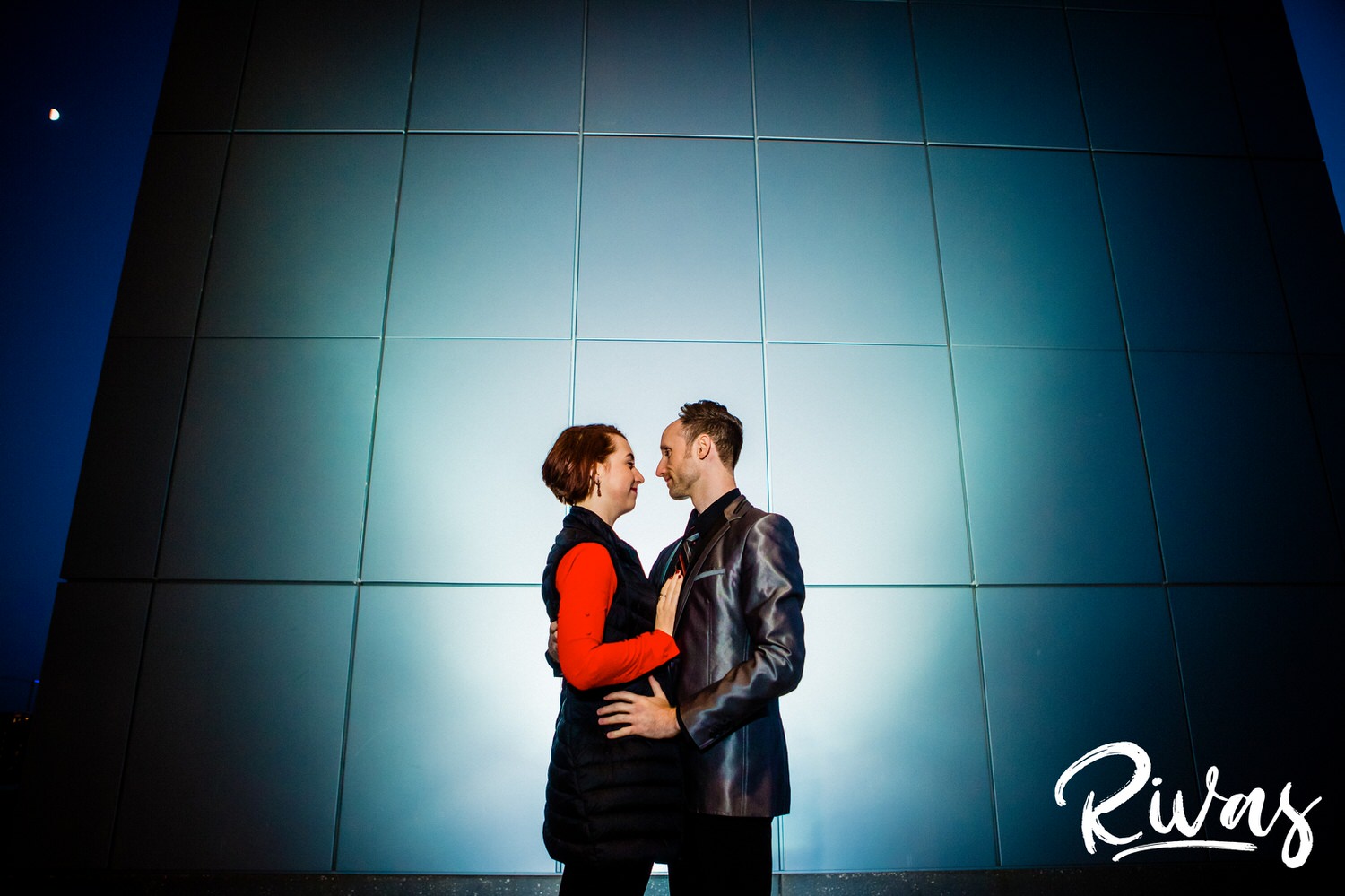 A vibrant picture of an engaged couple sharing an embrace as they stand in front of a steel wall during their engagement session in Kansas City. 