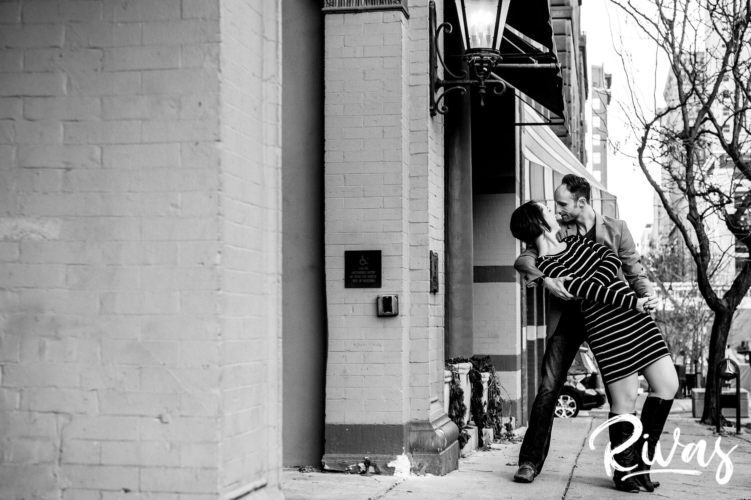 A candid black and white picture of an engaged couple dancing down the sidewalk of a street in Kansas City's Library District during their engagement session. 