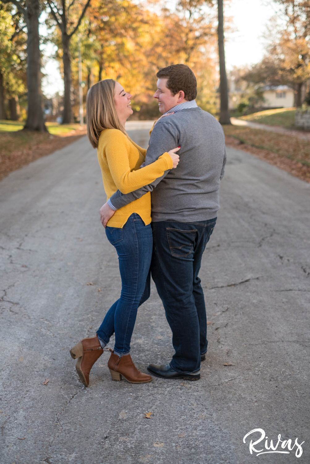 A candid picture of an engaged couple sharing an embrace and laughing together as they dance in the street during their engagement session in Kansas City. 