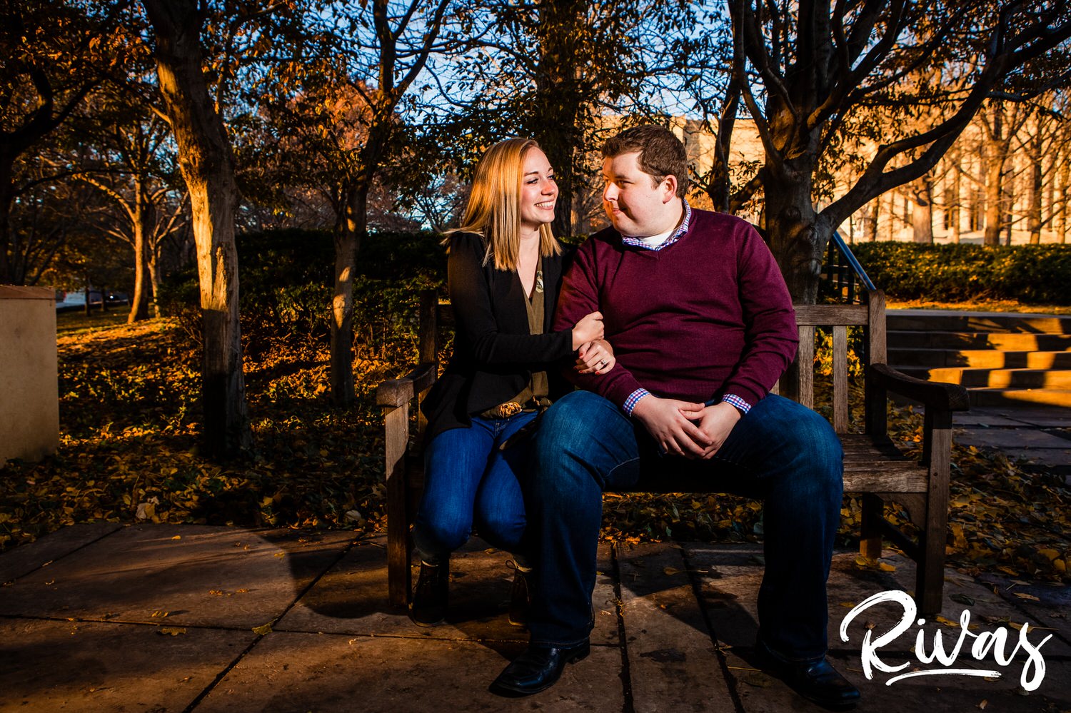 A candid picture of an engaged couple sitting on a bench snuggling during their engagement session at The Nelson Atkins Museum of Art in Kansas City. 
