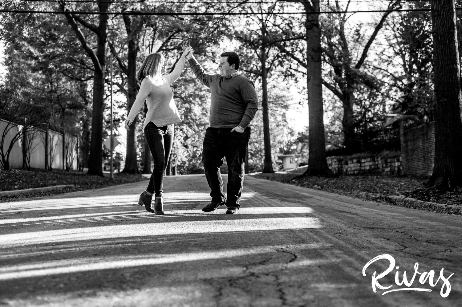 A candid black and white picture of a couple walking and dancing down the middle of a street during their engagement session in Kansas City. 