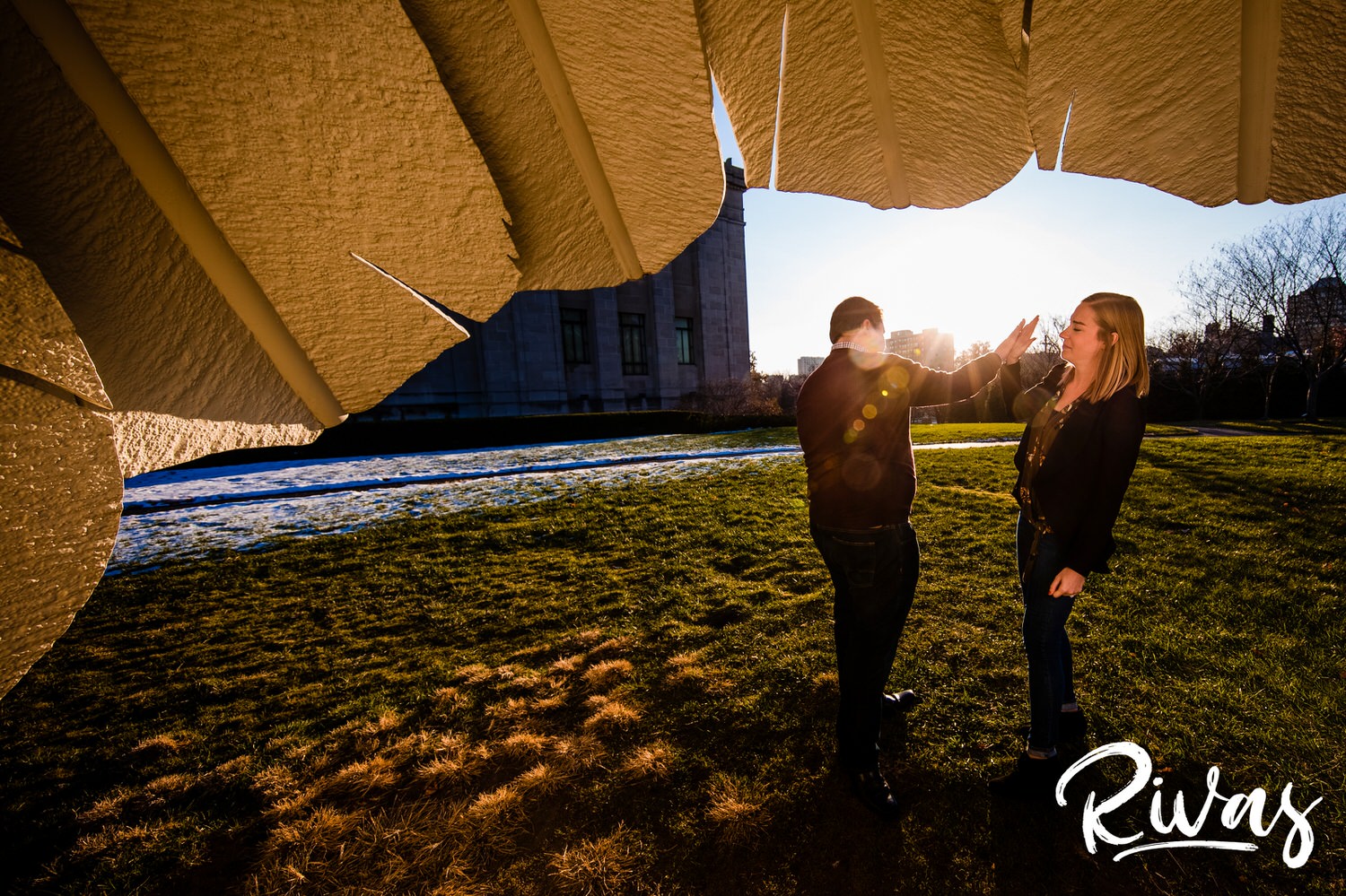 A candid picture of a couple high-fiving as they stand under a Shuttlecock at The Nelson during their engagement session in Kansas City. 