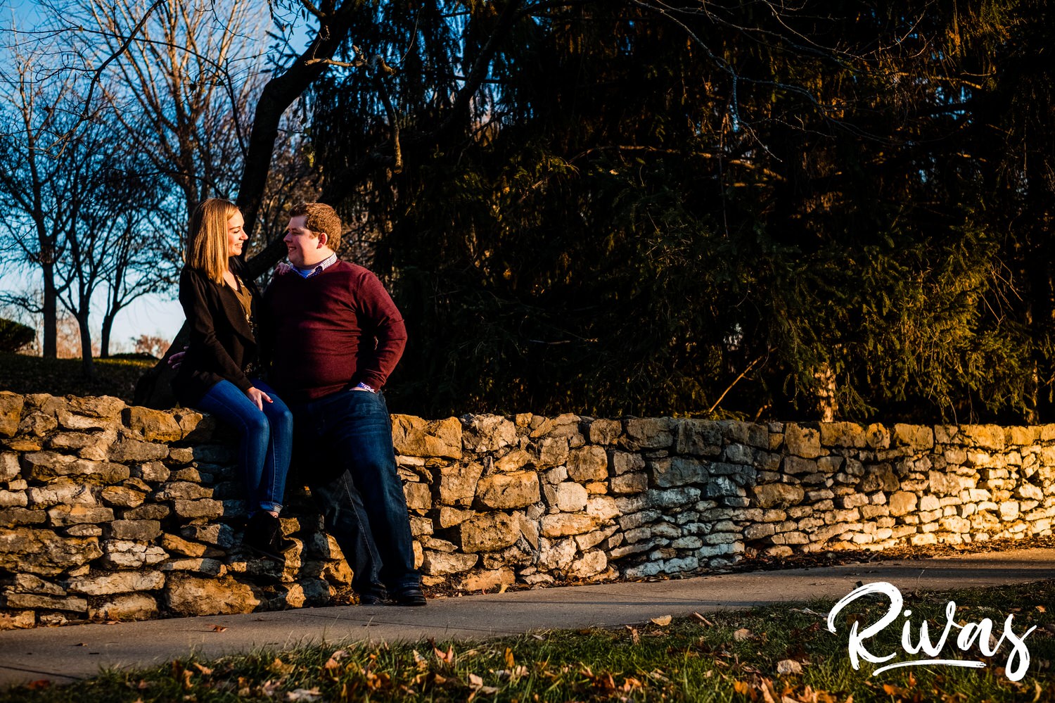 A candid picture of a couple sitting on the stone wall outside The Nelson Atkins Museum of Art during their engagement session in Kansas city. 