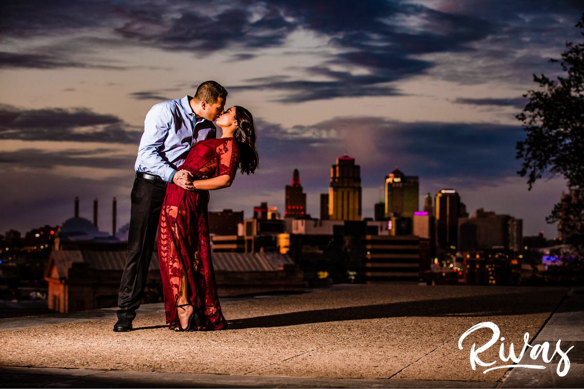 Stylish Kansas City Engagement Session | A photo of an engaged couple sharing a kiss in front of the Kansas City skyline as the man dips the woman during their sunset engagement session.