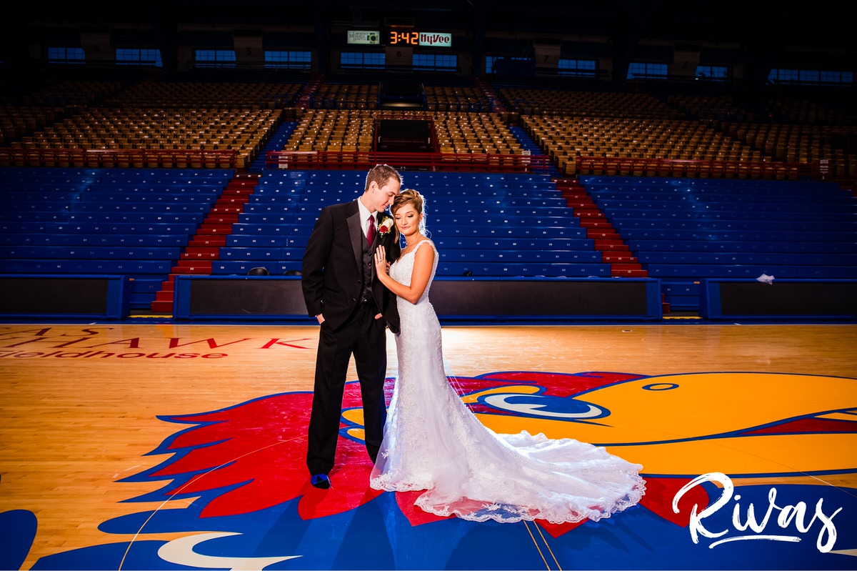 Fun Filled Wedding in Lawrence | Destination Wedding Photographers | A photo of a bride and groom sharing an embrace while standing barefoot on center-court of Allen Fieldhouse on their wedding day in Lawrence, Kansas.