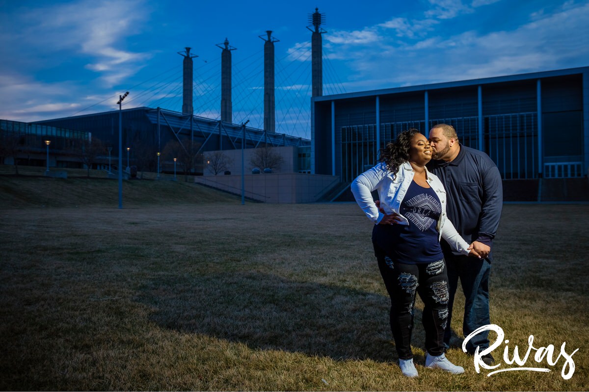 Downtown Kansas City Engagement Sneak Peek | Rivas | Kansas City Wedding Photographers | A photo of an engaged couple standing on the lawn of the Kansas City Convention Center with the four spires in the background during their evening engagement session.