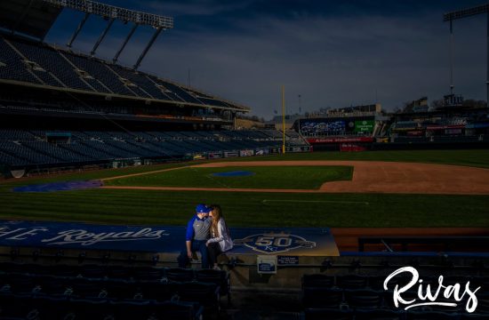Spring Kauffman Stadium Engagement Pictures | A wide-shot of an engaged couple sitting on top of the Royal's dugout at Kauffman Stadium during their Kansas City Engagement Session.