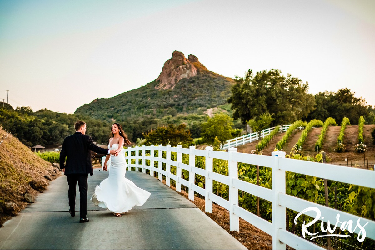 Romantic Vineyard Wedding Sneak Peek | Destination Wedding Photographers | A candid photo of a bride and groom dancing while walking down the road at Malibu's Saddlerock Ranch at sunset on the evening of their wedding.