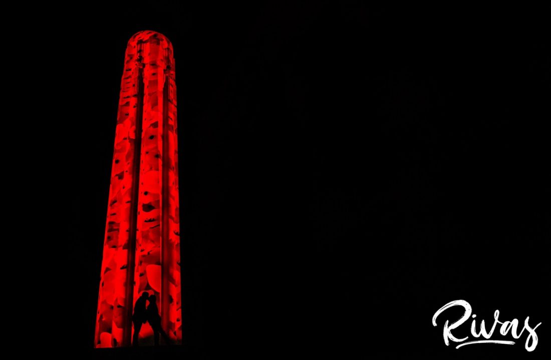 Nighttime Liberty Memorial Engagement Sneak Peek | KC Wedding Photographers | Rivas | A silhouetted portrait of an engaged couple sharing an embrace in front of the pipe at Liberty Memorial, lit up with poppies in remembrance and celebration of the Armistice Centennial Event in Kansas City.