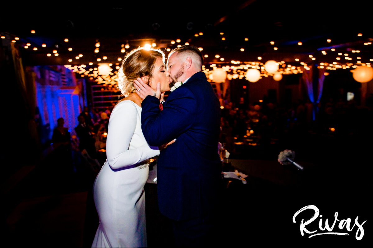 A candid picture of a bride and groom sharing a kiss as they stand on the stage of 28 Event Space during their wedding reception. | Kansas City Room Wedding & Reception | Rivas Weddings