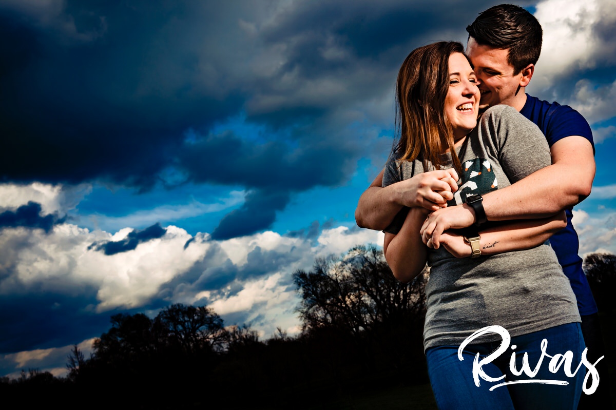 A colorful, playful picture of an engaged couple laughing and hugging against a colorful sky in the background during their engagement session in Kansas City's Loose Park. 