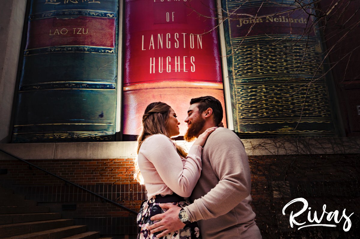 A colorful picture of an engaged couple standing in front of the infamous Kansas City Library parking garage sharing an embrace during their engagement session. 