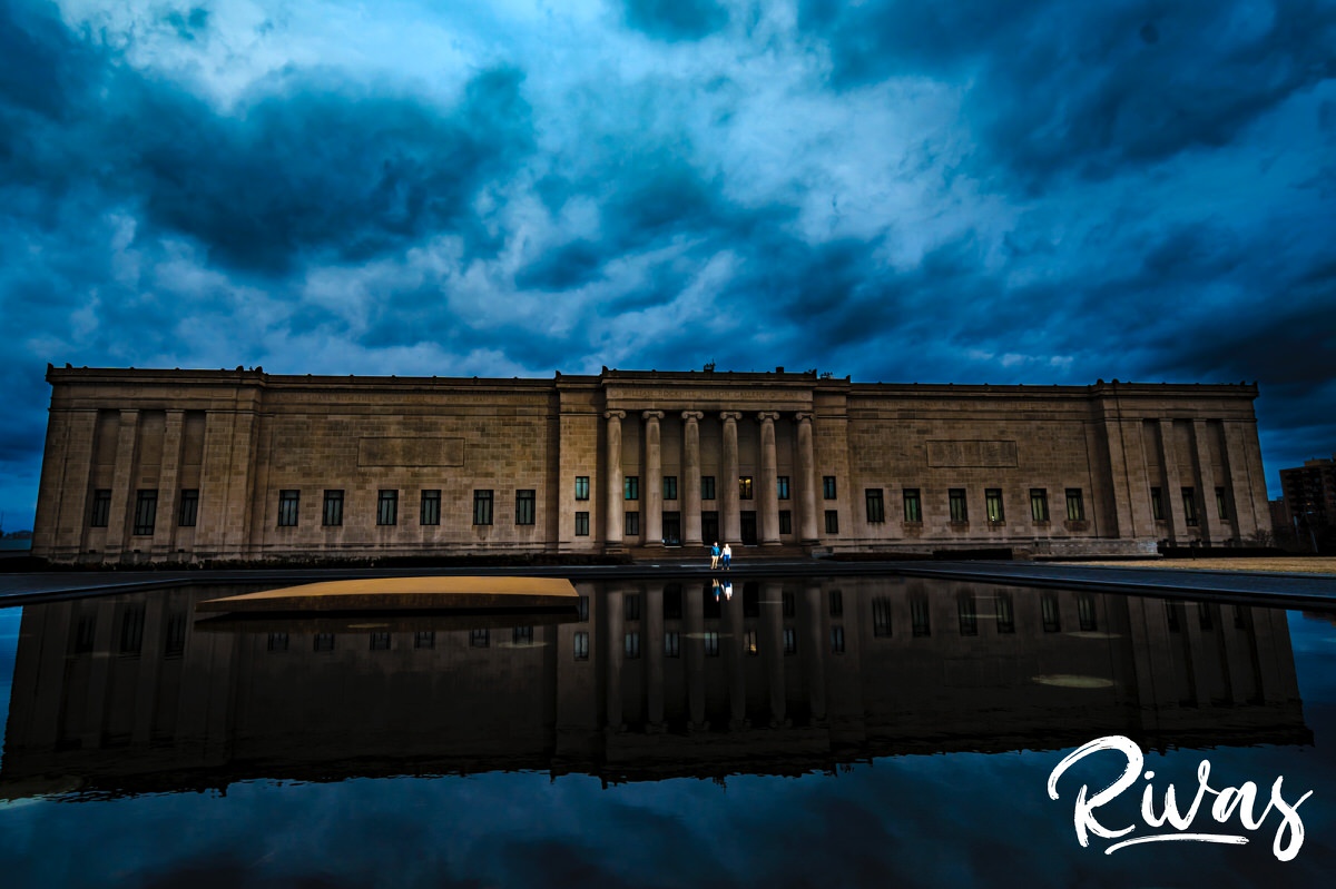 A dramatic portrait of a couple standing on the edge of the reflecting pool at The Nelson Atkins Museum of Art as stormy clouds roll overhead. 